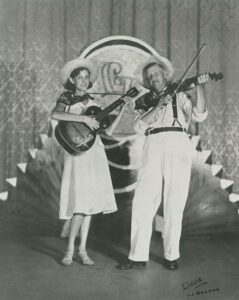 Fiddlin’ John Carson and his daughter, Moonshine Kate, performing on stage in matching straw hats and vintage attire, circa 1927.