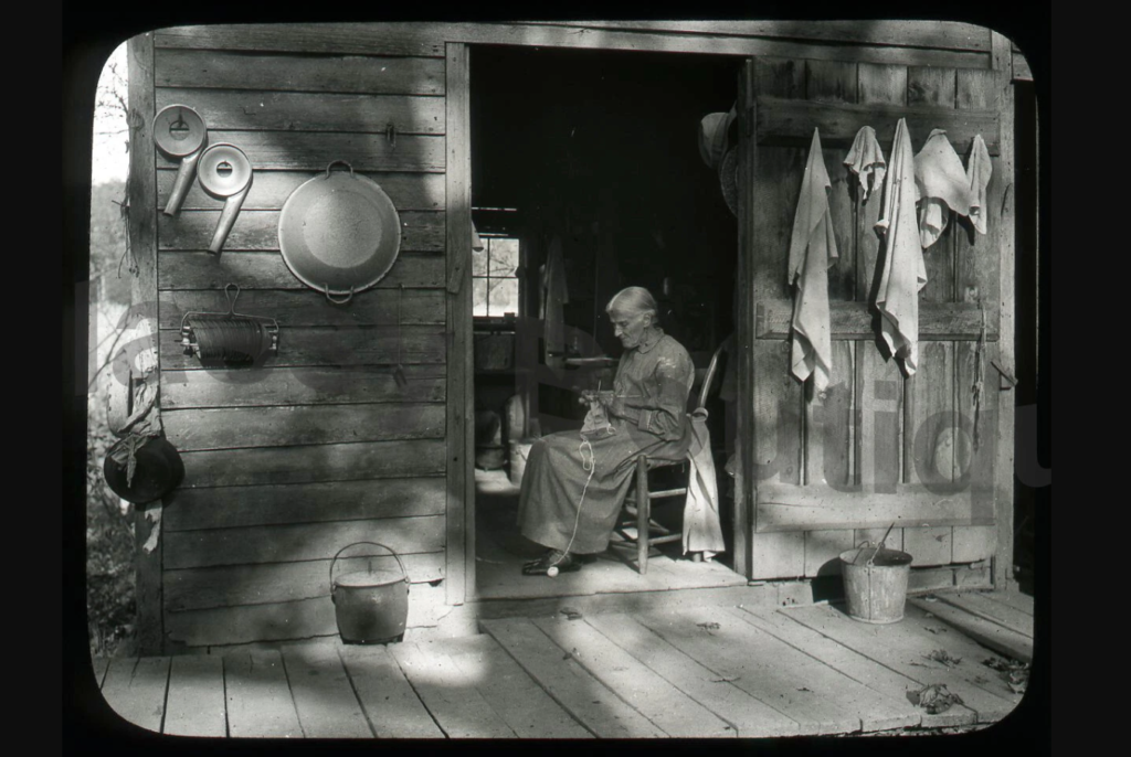 Elderly woman crocheting on a wooden porch of a rural Appalachian cabin, 1930s