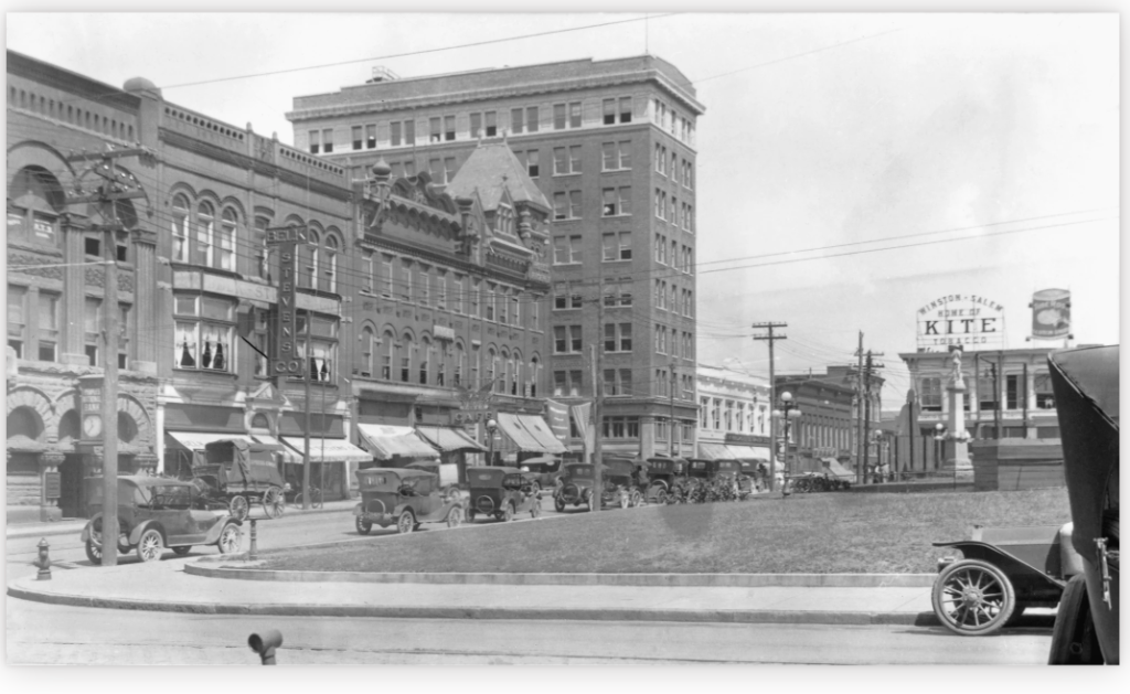 Historic black-and-white photograph of Court House Square, Winston-Salem, North Carolina, circa 1925, showing vintage automobiles, brick storefronts, and the Kite Tobacco billboard in the distance.