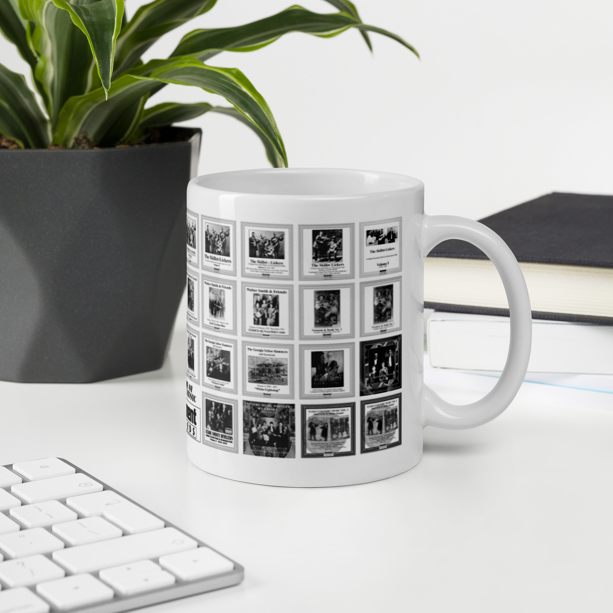 White mug printed with vintage album covers from Document Records sits on a white desk beside a keyboard, a plant, and a stack of books.